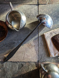 (Modern colonial-style handmade ladle combining polished and forged stainless steel elements.)