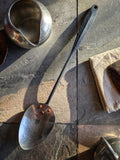 (Hand-forged stainless steel serving spoon with a black-forged handle and polished hammered bowl.)