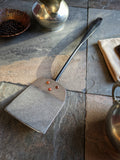 (Close-up of a hammered stainless spatula blade riveted with copper, hand-forged in Quebec.)