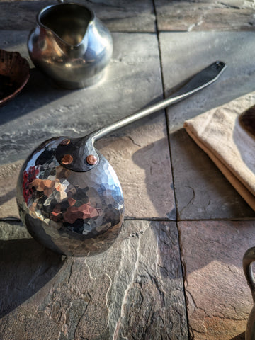 (Hand-forged stainless steel ladle with a black-forged handle and hammered polished bowl.)