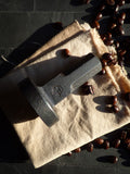 full view of hand forged espresso coffee tamper resting on its side on a cloth with coffee beans around