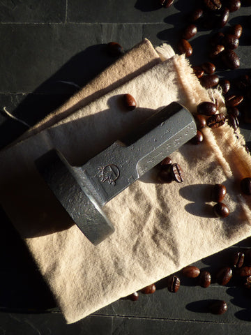 full view of hand forged espresso coffee tamper resting on its side on a cloth with coffee beans around