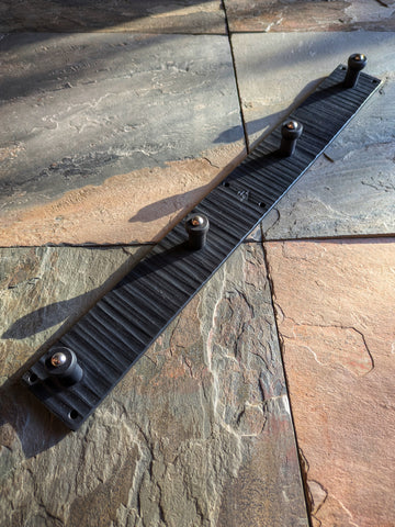 Angled close-up of a handcrafted carbon steel peg hook rack with four pegs and wax-sealed black forge finish, made at Strobus Forge.