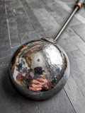 Close-up of a polished hammered stainless steel bowl on a handcrafted sauna ladle with copper rivets.