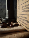 alternate view of hand forged coffee tamper with tamper blurred in the distance and focus being made on the words "hand forged by Strobus Forge Québec, Canada" on box
